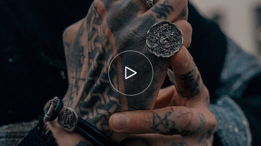 Tattooed hand with intricate silver rings.